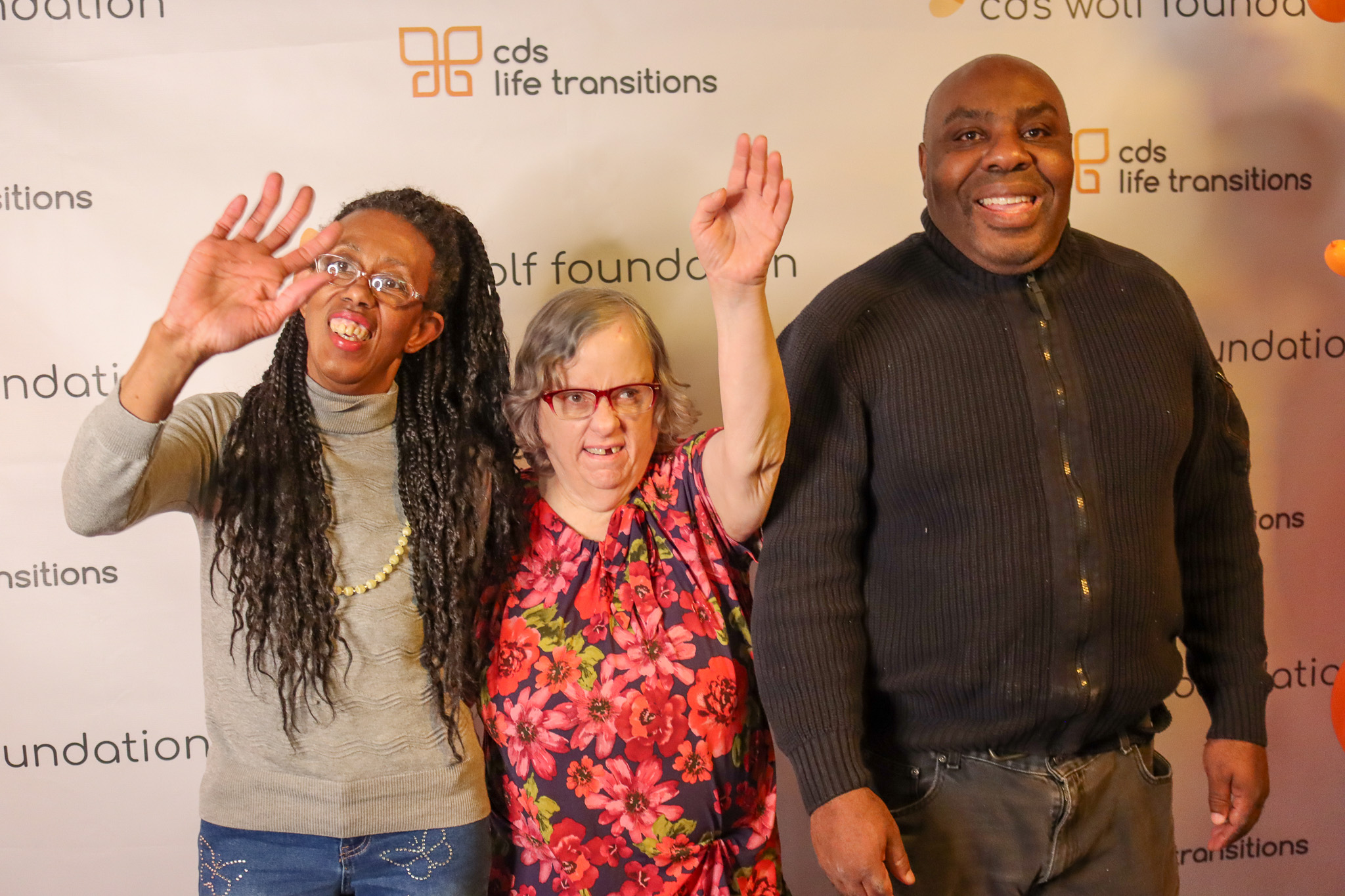 2 women and 1 male standing in front of a cds life transitions backdrop. The women have their hands raised to the air all smiling at the camera.