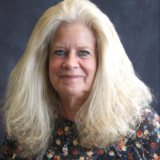 Jayme Sharpe, Director of Person Centered Services in a floral shirt sitting in front of a dark gray wall.